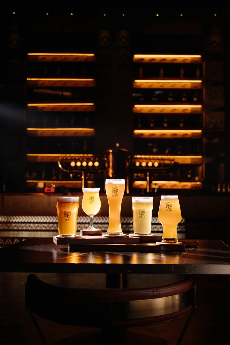 Five Akan beer glasses lined up in front of the warmly lit brewery bar