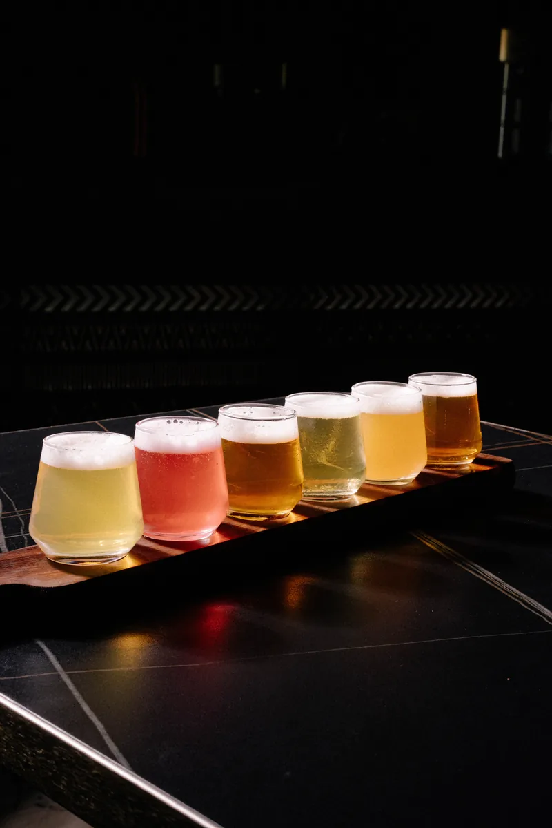 Six glasses of different house pours on a wooden tasting paddle at Akan